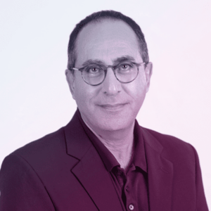 A middle-aged man with short dark hair, glasses, and a slight smile, wearing a dark blazer over a collared shirt, poses against a plain light background—ideal for discussing cyber crime on the Cyber Crime Junkies Podcast.